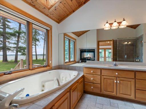The lakeside primary bath features a jetted soaking tub, dual-sink vanity, walk-in tiled shower, and a two-sided fireplace for a true retreat experience.