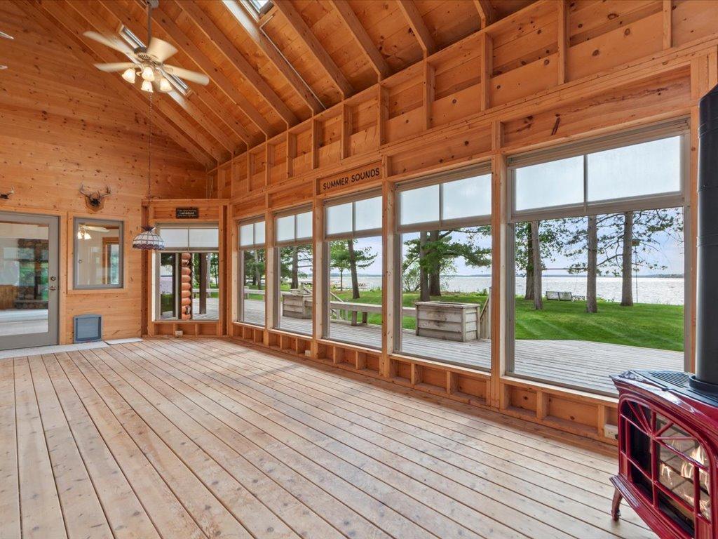 The vaulted three-season porch features soaring wood-lined ceilings, a gas stove, and walls of windows framing beautiful lake views.