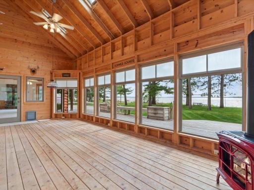 The vaulted three-season porch features soaring wood-lined ceilings, a gas stove, and walls of windows framing beautiful lake views.