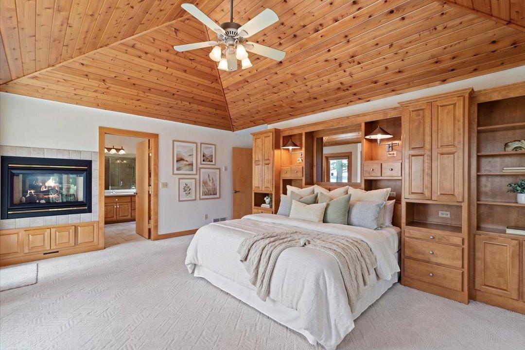 Virtually Staged. The spacious main-level primary suite features vaulted wood ceilings, custom built-ins, a two-sided fireplace, and a private ensuite bath.