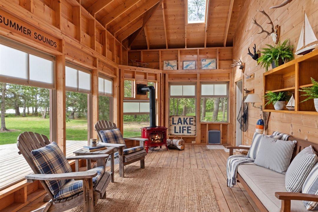 Virtually Staged. The vaulted three-season porch offers a spectacular setting to enjoy lake breezes, morning coffee, and evenings by the gas fireplace surrounded by nature.