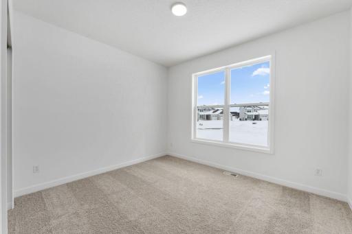 Overlooking the front of the home, this secondary bedroom enjoys natural light streaming in through its tall windows. It includes plush carpeting and a wardrobe closet.