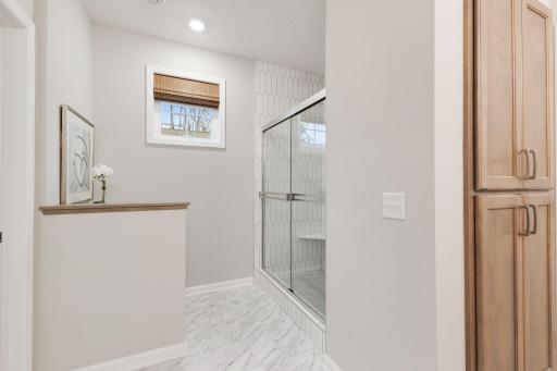 Actual home's primary bath features a beautiful, glossy tiled shower and glass pivot door.