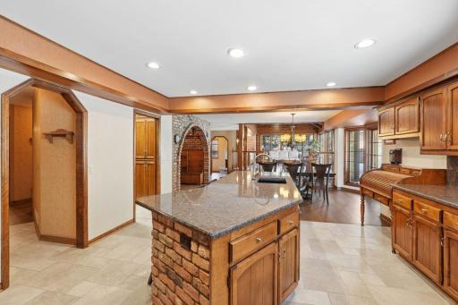 âBright kitchen with warm wood cabinetry, a brick-accented island, generous counter space, and direct access to a walk-in butlerâs pantry, with open views to the dining area and brick alcove.â