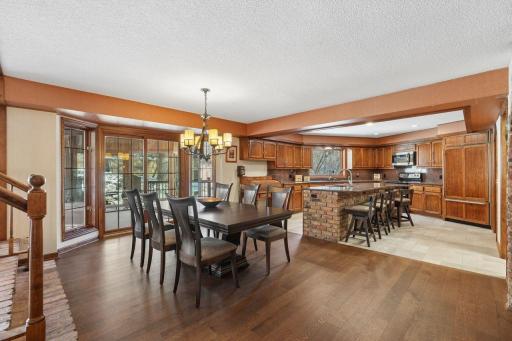âBright dining area with large windows and warm wood floors opens seamlessly to the spacious kitchen, featuring rich cabinetry, brick accents, and a large center island perfect for gatherings.â