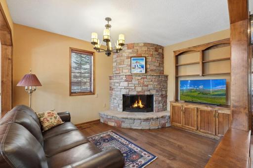 âCozy family room featuring a curved stone fireplace, warm wood built-ins, and rich hardwood flooringâperfect for relaxing or entertaining.â