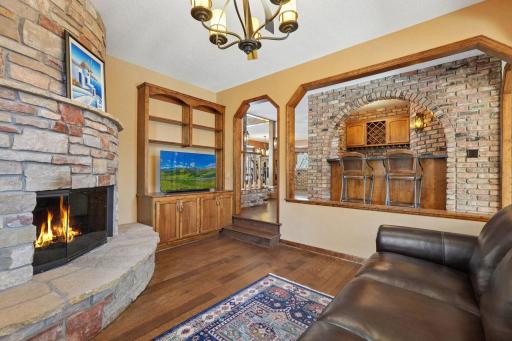 âCozy family room featuring a curved stone fireplace, built-ins, hardwood floors, and arched openings that overlook the brick bar areaâoffering warmth, character, and great flow for entertaining.â