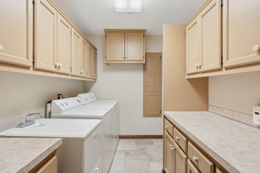 âSpacious laundry room with ample cabinet storage, large work counters, utility sink, and full-size washer and dryer, offering a bright and functional space for everyday tasks.â