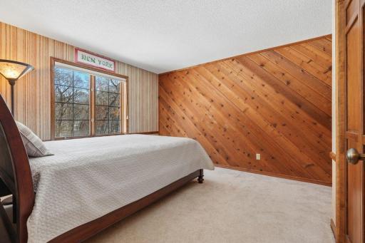 âBright bedroom with a large window overlooking the treetops, featuring warm wood-accent walls, neutral carpeting, and ample space for a bed and additional furnishings.â