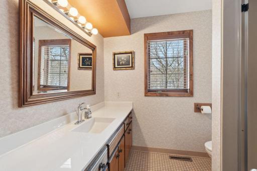 âBright bathroom featuring a long vanity with solid-surface top, large framed mirror, classic globe lighting, tile flooring, and a window that brings in great natural light.â