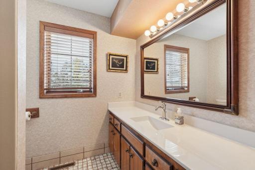 âBright full bath featuring a long vanity with updated countertop, large framed mirror, classic lighting, tile flooring, and two windows that bring in natural light.â