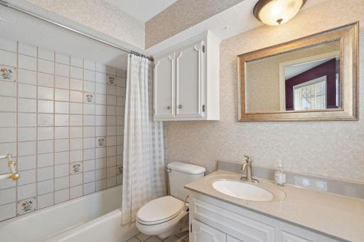 âBright ensuite bath featuring a tiled tub/shower combo with decorative accents, updated vanity with solid-surface top, framed mirror, and extra cabinet storage.â