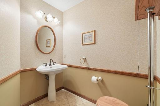 âConvenient half bath off the entrance featuring a pedestal sink, warm two-tone walls with wood trim, tile flooring, and classic lightingâideal for guests.â