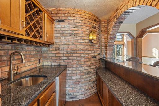 âBrick-arched bar off the family room, kitchen, and four-season porch, featuring wood cabinetry, granite counters, seating, a sink, and a built-in fridgeâperfect for effortless entertaining.â