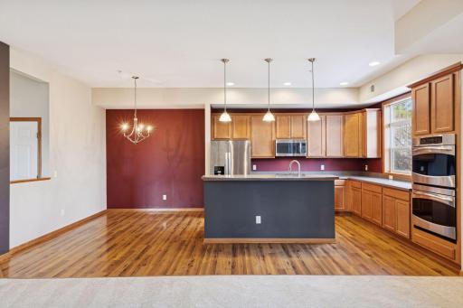 Open layout showcasing the oversized center island with breakfast bar seating, pendant lighting, and seamless flow into the dining space.