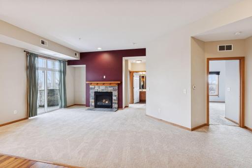 Bright living room with plush carpeting, stone-surround gas fireplace, and sliding glass door leading to a private balcony with scenic views.