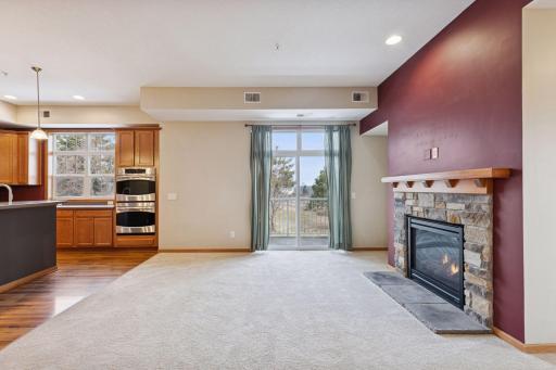 Bright living room with plush carpeting, stone-surround gas fireplace, and sliding glass door leading to a private balcony with scenic views.