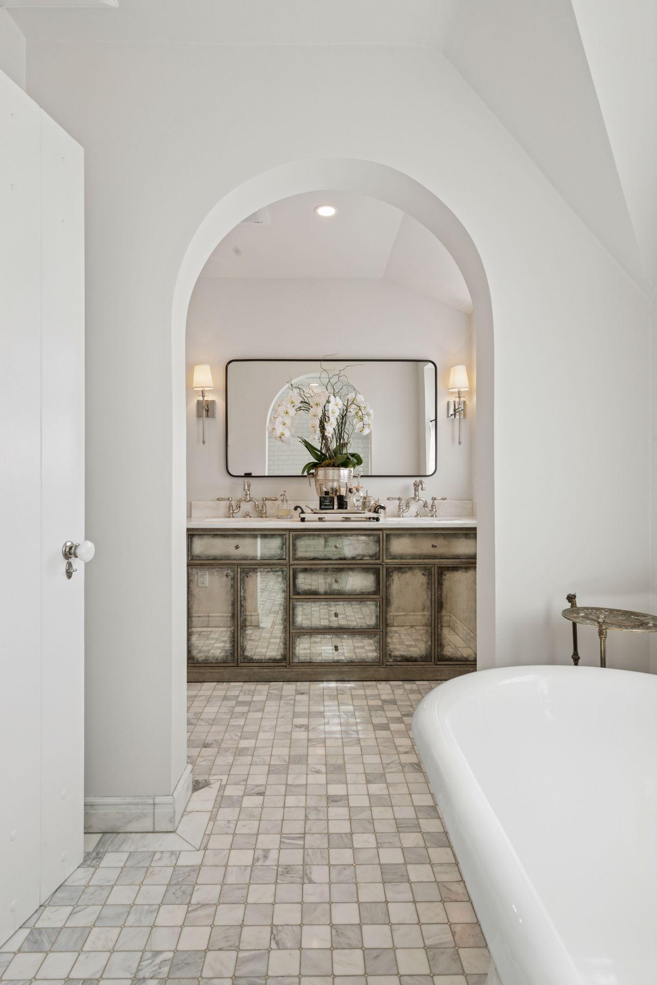 The beautifully designed primary bath features marble tile, a double vanity, arched doorway, elegant soaking tub, and walk-in shower.