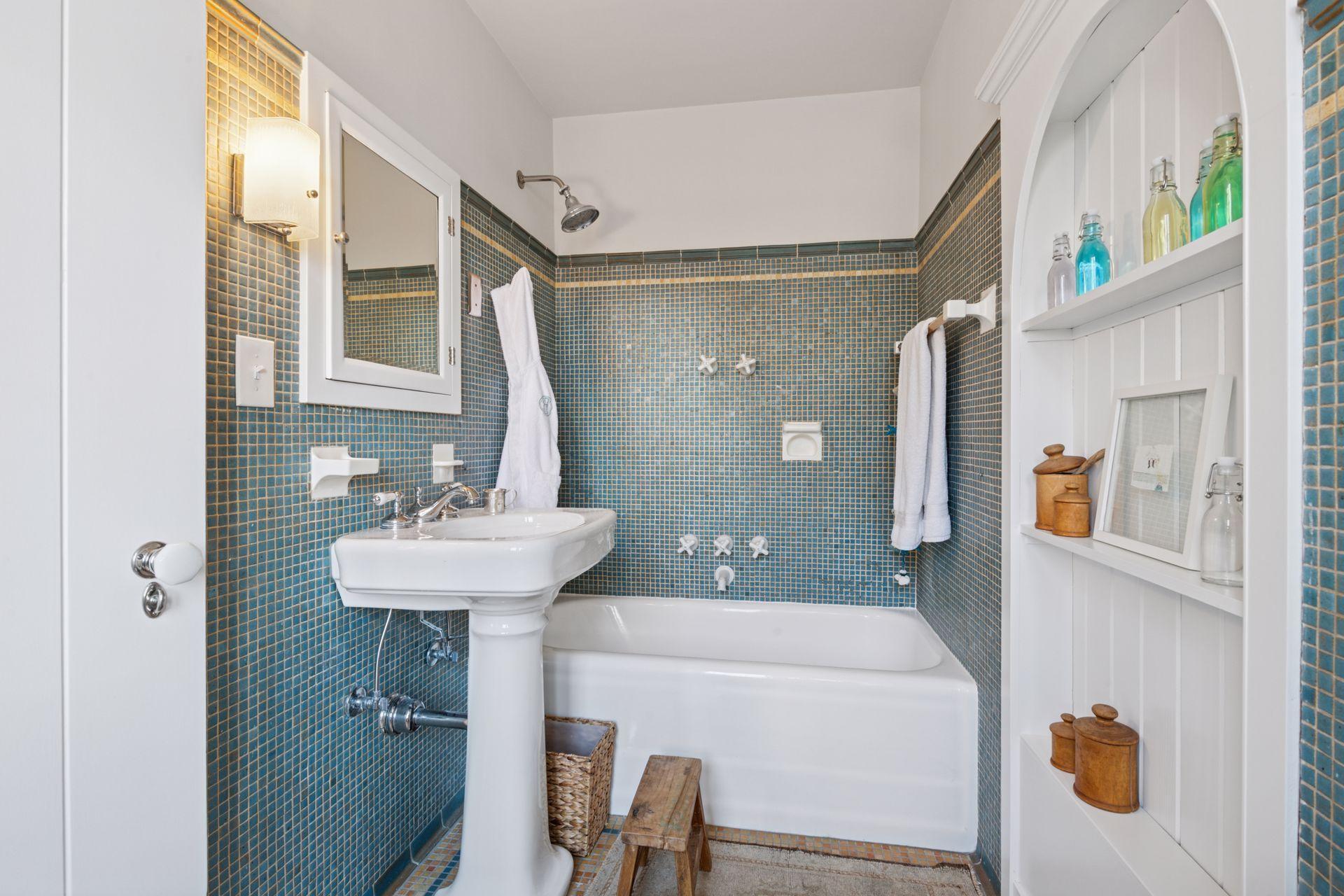 Third bedroom en suite bath with gorgeous original handmade tiles, medicine cabinet, built-in shelving, and a soaking tub with shower head.