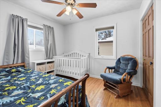 Bright secondary bedroom with hardwood floors, neutral walls, ceiling fan, and multiple windows providing natural light and a flexible space.