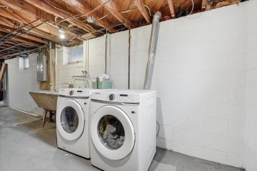 Laundry space with New (2024) front loader side-by-side washer and dryer, utility sink, and convenient lower-level location with room for additional storage. New 100 amp service in 2011.