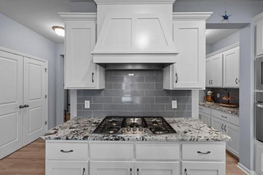 Quartz counters with cooktop, hood, tile backsplash, and slow-close drawers