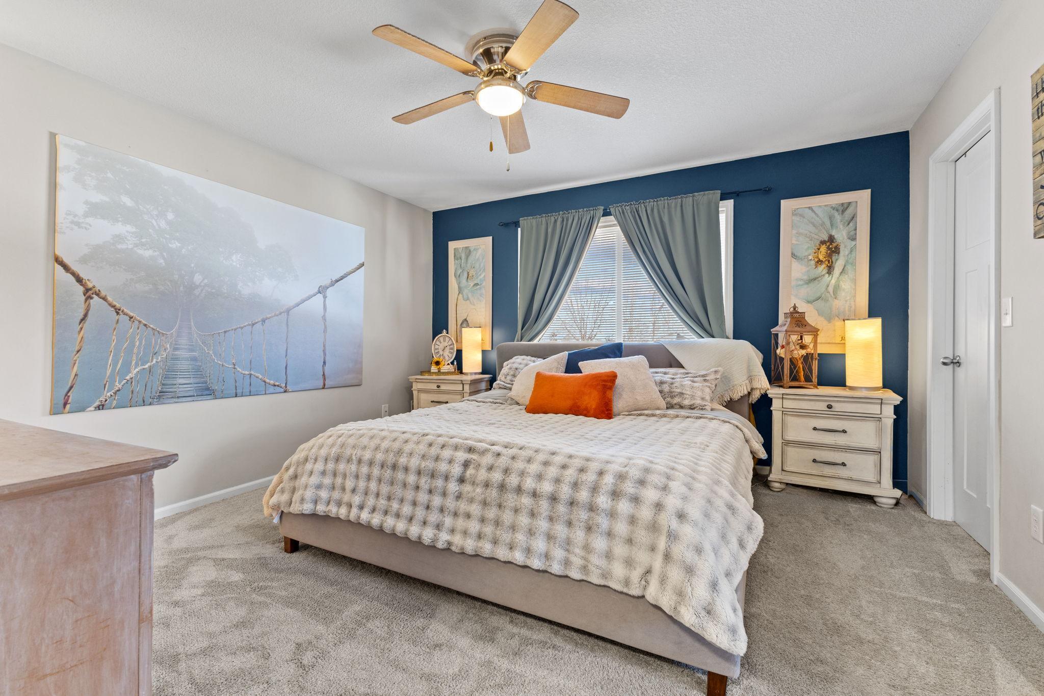The primary bedroom boasts neutral tones, plush carpeting, an oversized window and a ceiling fan for added comfort.