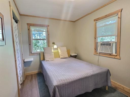 This cozy bedroom offers a quiet retreat with warm wood trim and natural light filtering through dual windows.