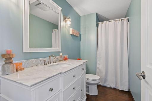 Beautifully updated lower-level Â¾ bathroom featuring a white dresser-style vanity with marble-finish countertops and tile floors.