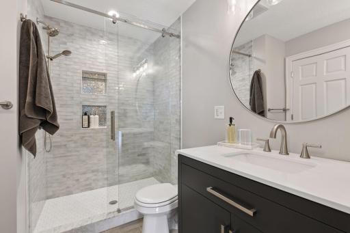 Beautifully updated bathroom featuring tile to the ceiling, a glass shower door, and a built-in niche for a clean, modern look. 2 separate vanities in the primary bathroom and 2 separate closets.