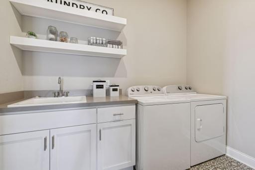 Laundry room is perfectly located from the primary bedroom and bathroom which is great for doing your laundry! Sink in the room with cabinet space for storage and shelving for organization as well.