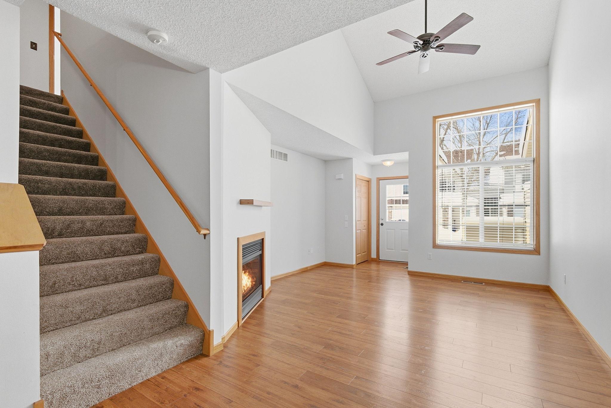 Spacious and inviting vaulted great room with cozy gas fireplace, ceiling fan, double high windows, open to dining room.