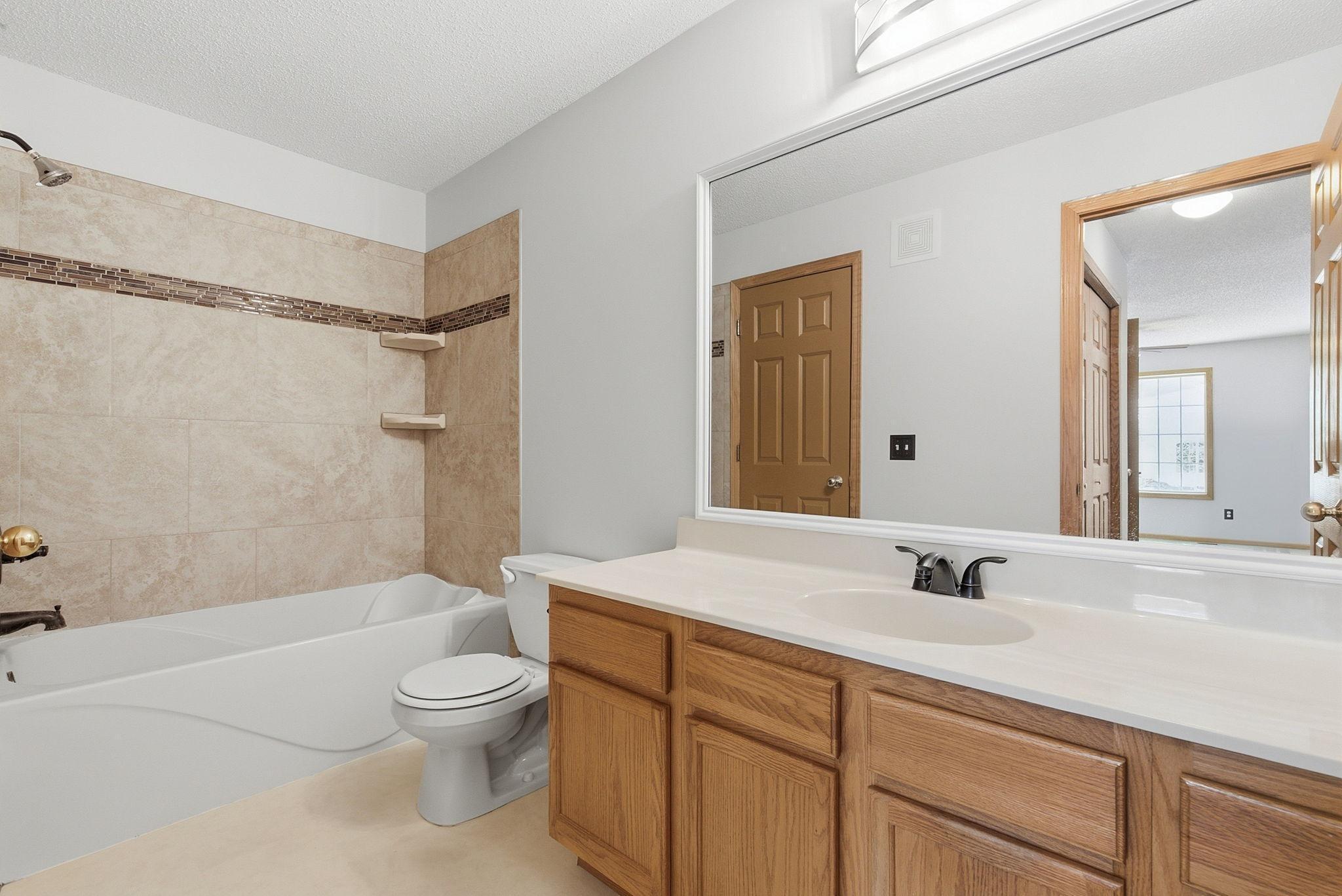 Upper level full bathroom with deep bathtub and decorative tile shower surround, linen closet with shelf.