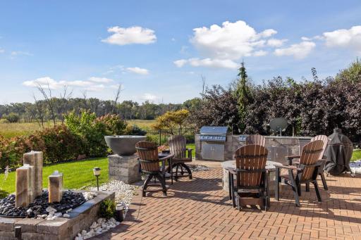 A sprawling paver patio features a built-in gas firepit, a bubbling water fountain, and a dramatic firebowl.