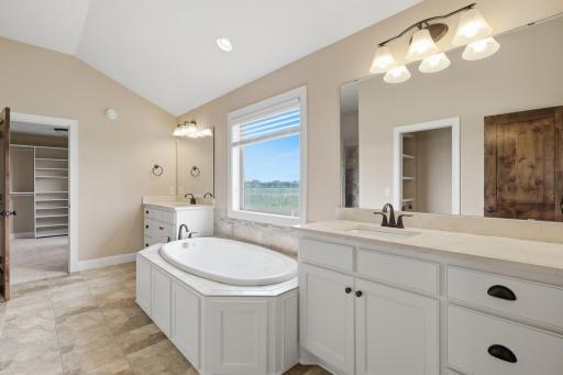 A spa-like bath featuring dual vanities, a jetted tub, a beautifully tiled walk-in shower, a private water closet, and heated tiled floors.