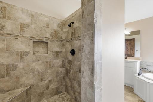 Walk-in shower with two shower heads, bench, and wall shelf.