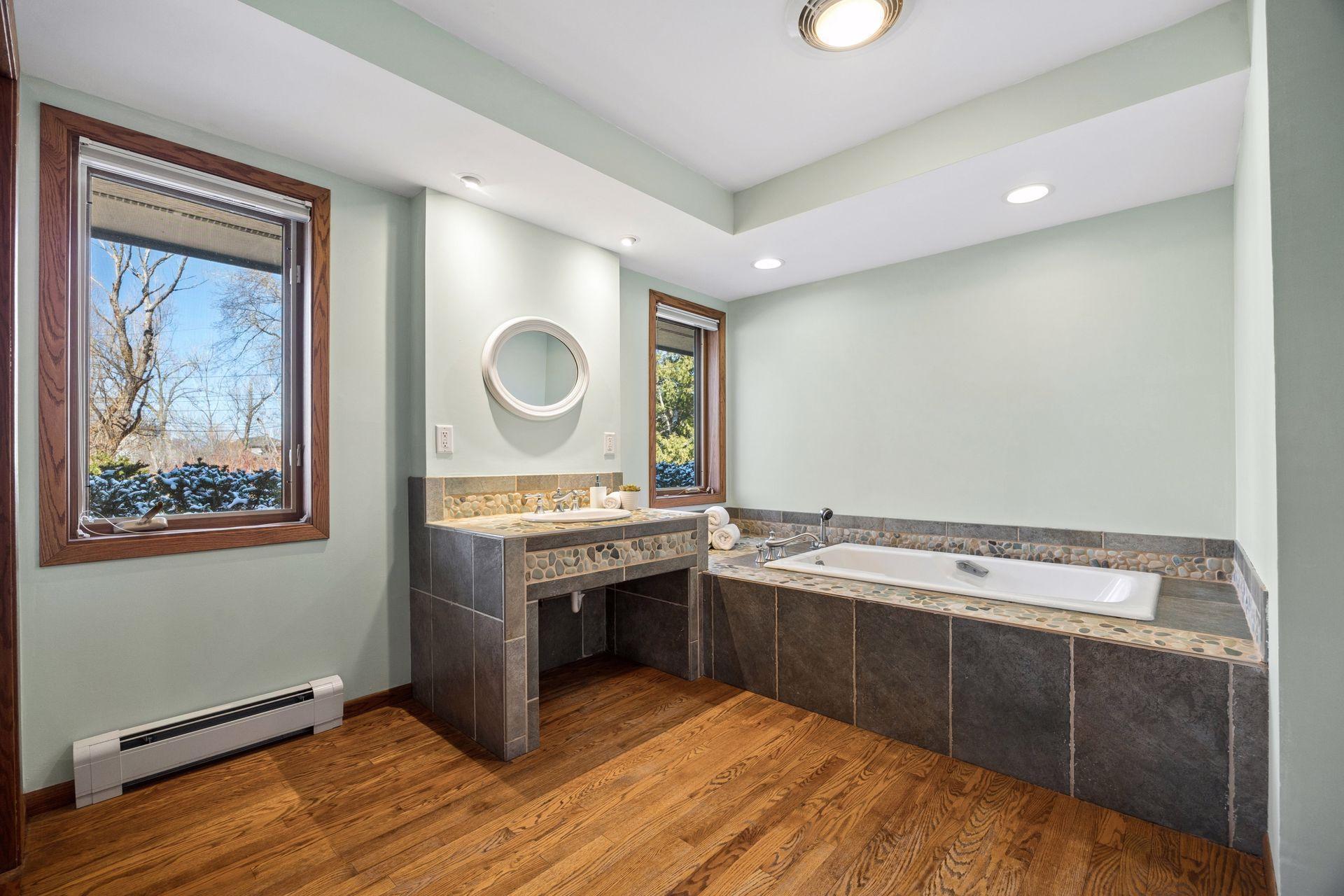 Large hall bath with wood floors and stone tile tub surround.