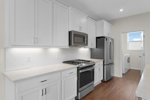 White cabinetry, quartz countertops, tile backsplash and stainless steel appliances.