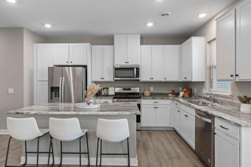 The kitchen is beautifully appointed with crisp white cabinetry, sparkling granite countertops, stainless steel appliances, and a large center island with breakfast bar seating.