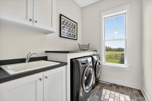 Functional laundry space with side-by-side washer and dryer, sink, cabinetry, and a window for natural light on the main level.