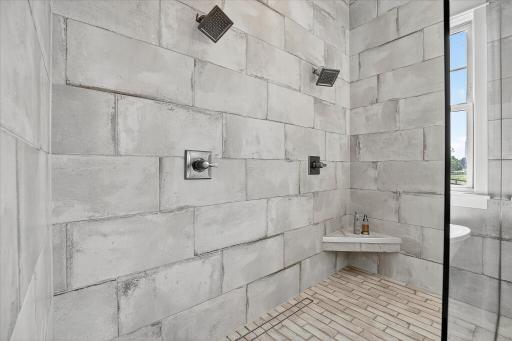 Expansive tiled shower with multiple showerheads and built-in bench seating.