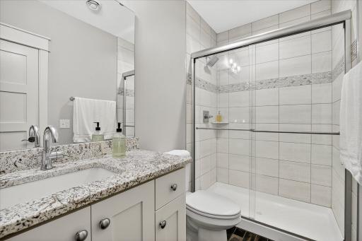 3/4 bathroom featuring granite countertops, white cabinetry, and a glass-enclosed tiled shower.