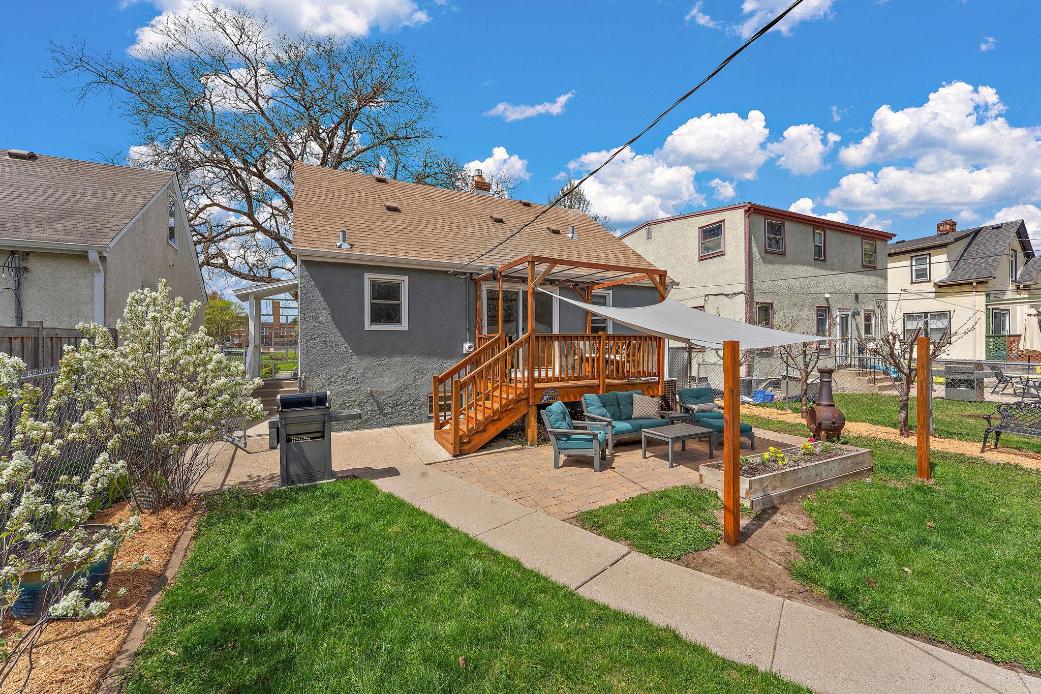 Picturesque back yard with paver patio, deck, and a myriad of perennial plants and fruit-producing bushes and trees. To the left in this photo are serviceberry bushes just starting to bloom!