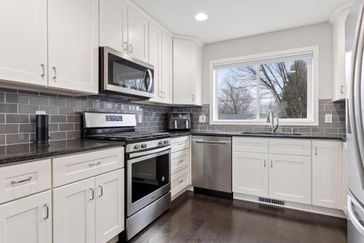 Sleek and modern kitchen featuring granite counters, subway tile backsplash, full size cabinetry with crown molding, and stainless appliances.