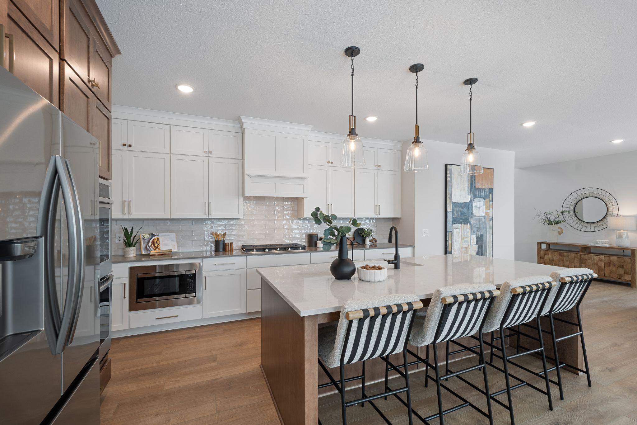 Elite kitchen with huge island with wing walls, double ovens, gas range and custom hood vent, floor to ceiling cabinetry and walk-in pantry