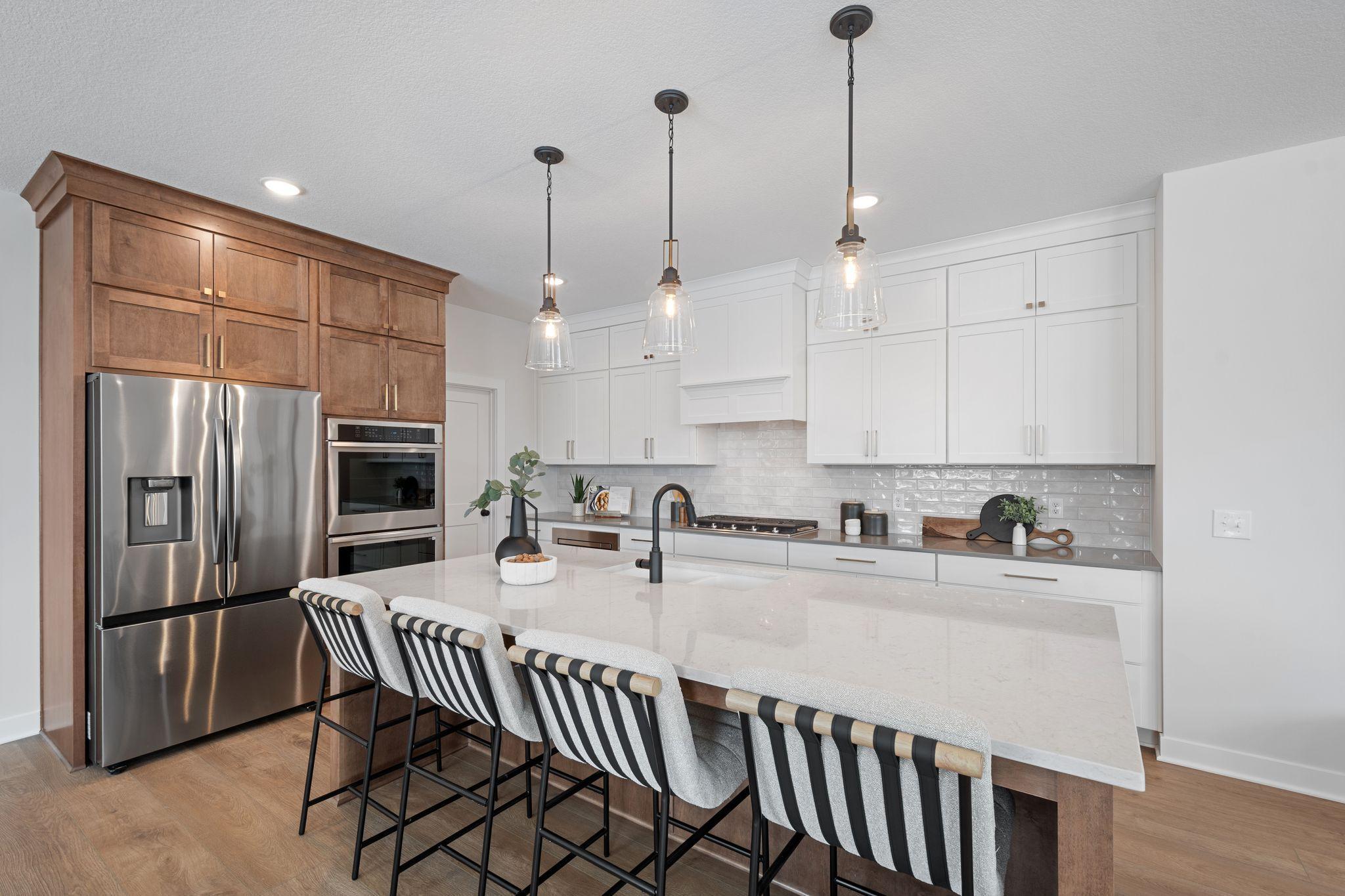 Elite kitchen with huge island with wing walls, double ovens, gas range and custom hood vent, floor to ceiling cabinetry and walk-in pantry