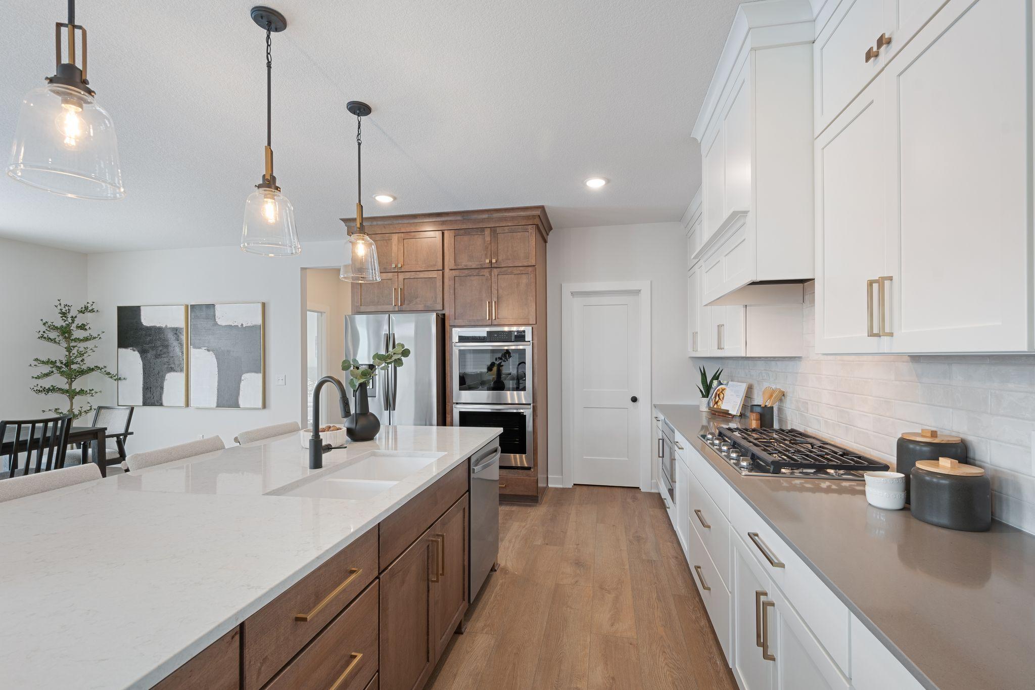 Elite kitchen with huge island with wing walls, double ovens, gas range and custom hood vent, floor to ceiling cabinetry and walk-in pantry