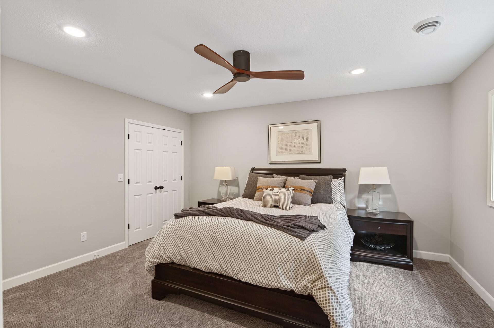 This cozy bedroom includes recessed lighting and a ceiling fan, mirroring the finishes found throughout the lower level.