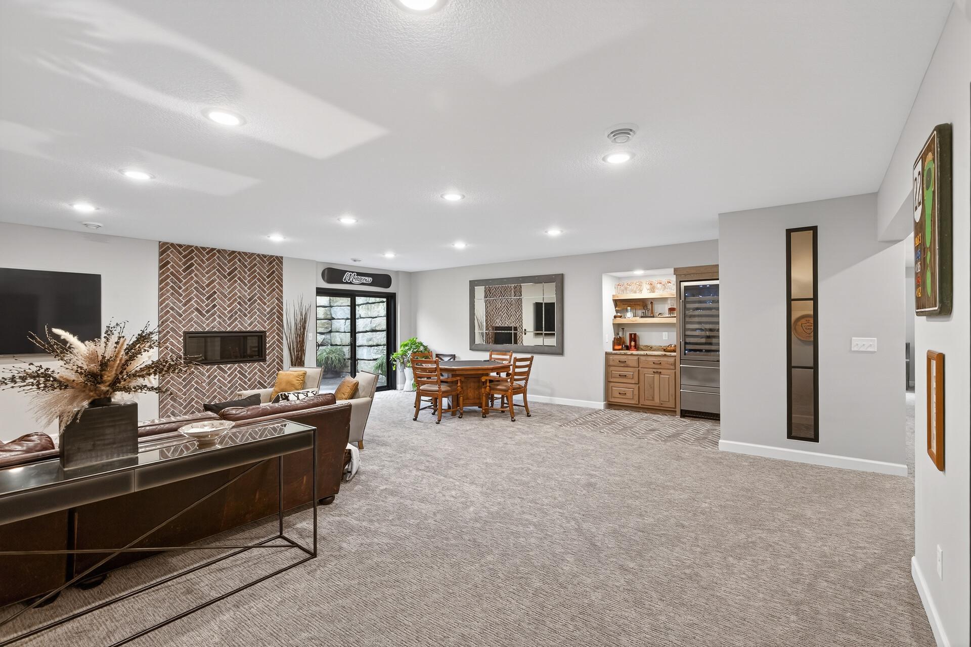 The remodel included a walk-out addition to the basement along with extensive landscaping improvements. A sleek, floor-to-ceiling tiled wall frames a modern fireplace, anchoring this bright lower-level living space.