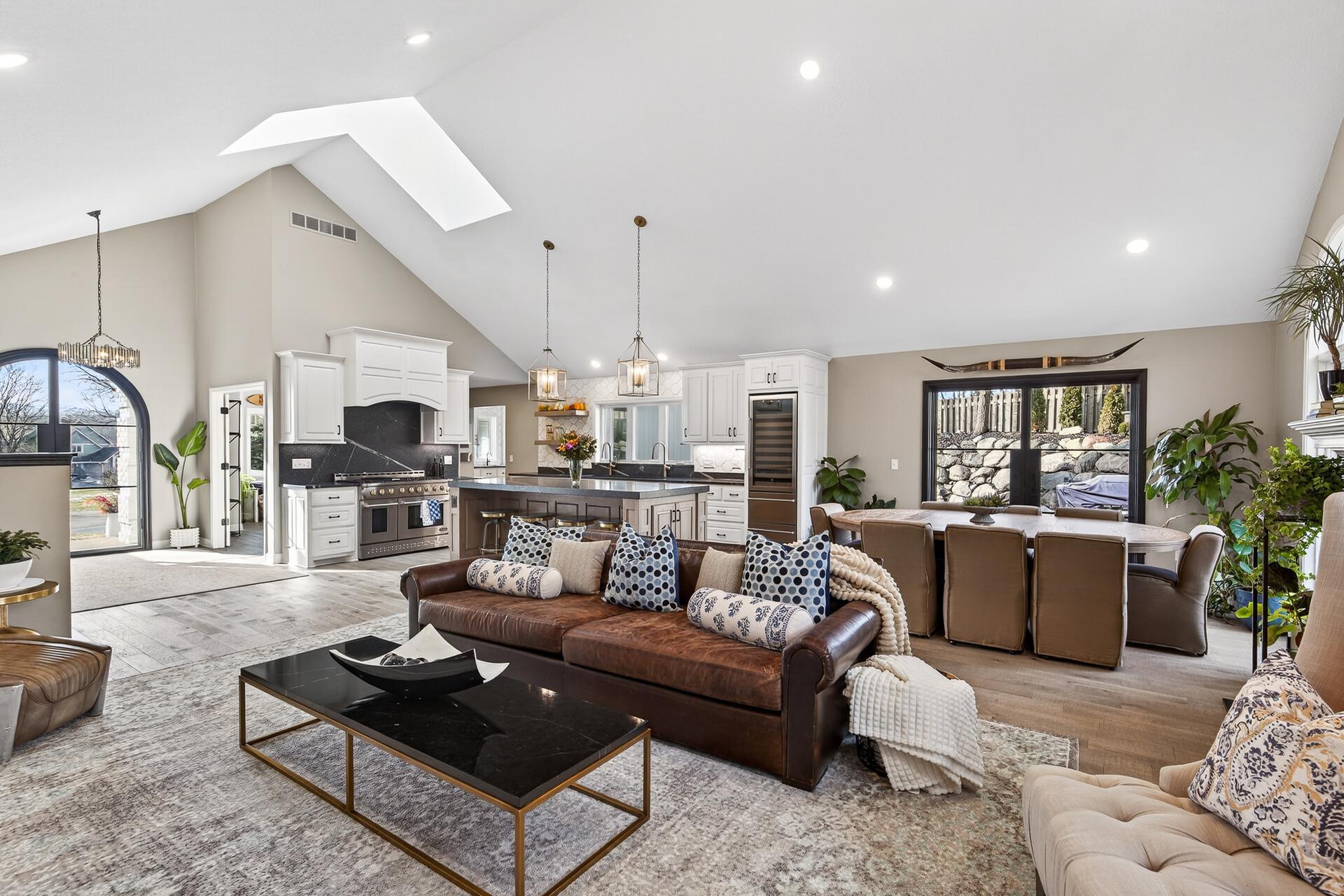 A breathtaking panoramic view from the living room, capturing the soaring vaulted ceilings that showcase the arched entry doors, gourmet kitchen, and sun-drenched dining area.